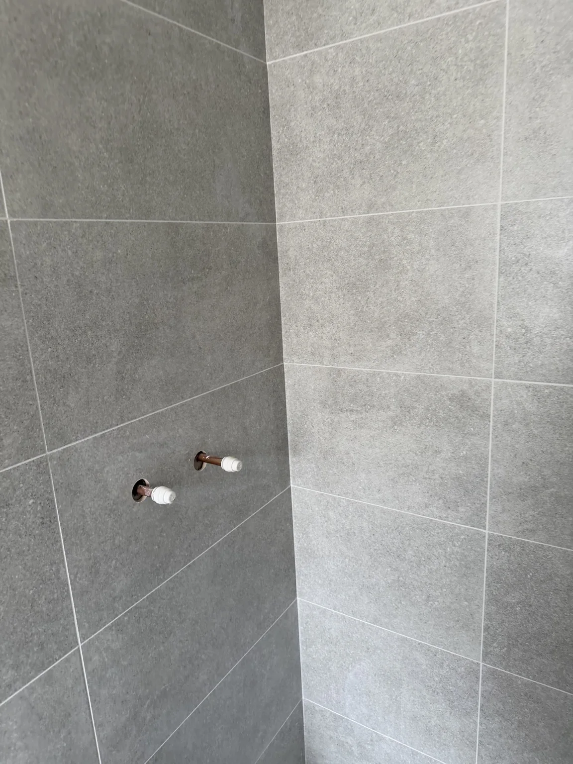 Neat pipe cuts through grey shower tiles
